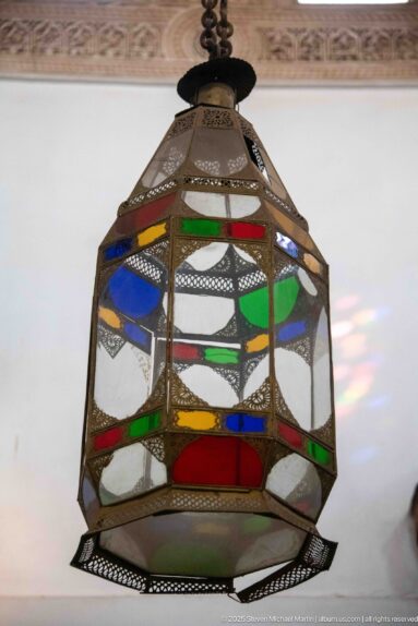 Faceted metal lantern with blue, green, red and yellow glass panels hanging inside Bahia Palace.
