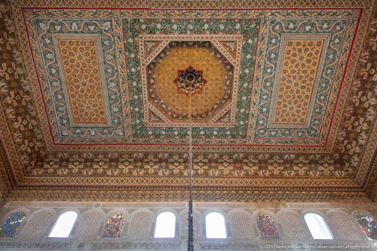 Painted Bahia Palace ceiling with central octagonal star medallion and colored-glass windows along the wall below.