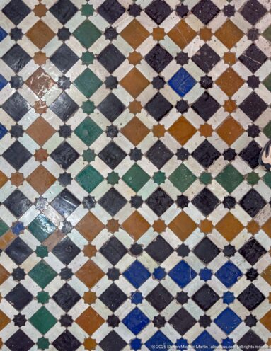 Close view of Bahia Palace floor tiles arranged in black, white, green, ochre and blue diamonds.