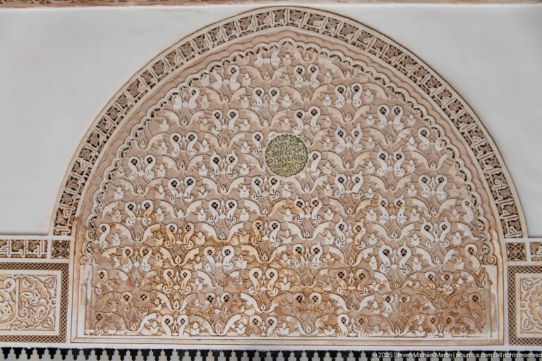 Arched carved stucco panel filled with dense vegetal arabesques and a small circular medallion at the center.