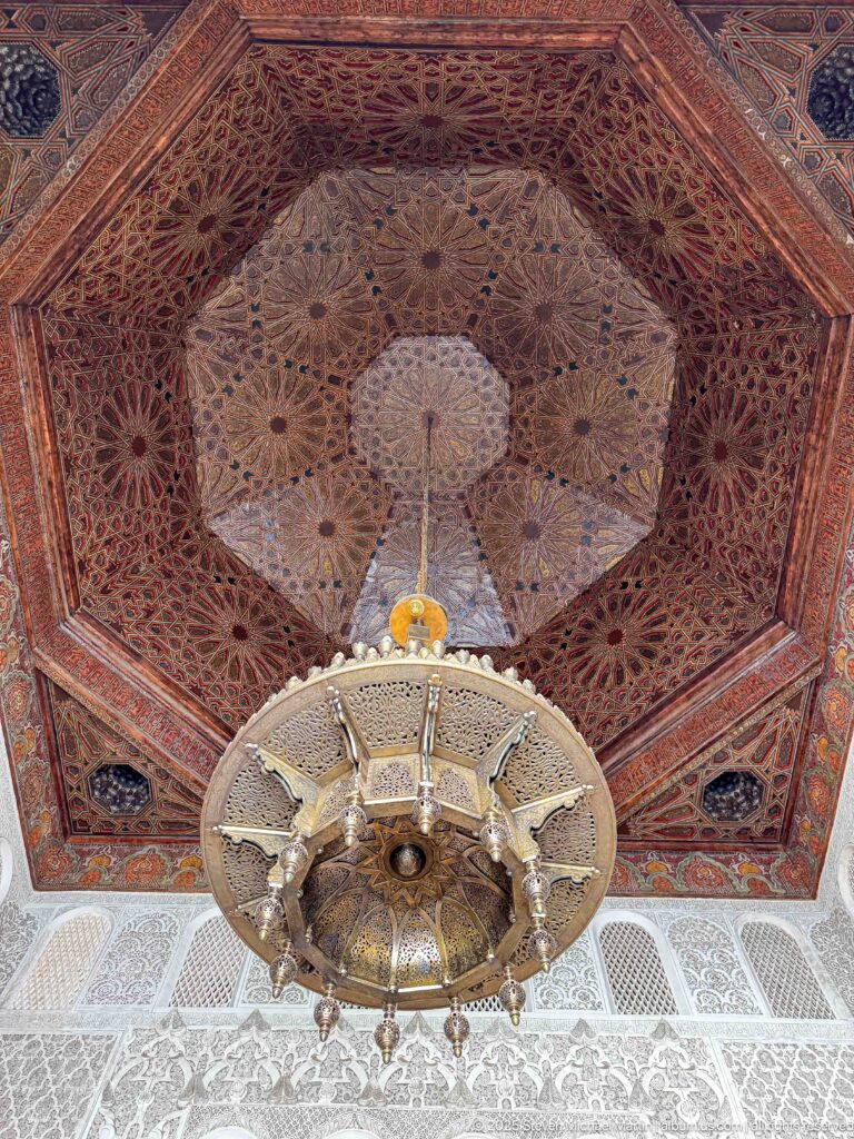 Faceted carved wooden ceiling with radiating geometric patterns above a large suspended metal lantern.
