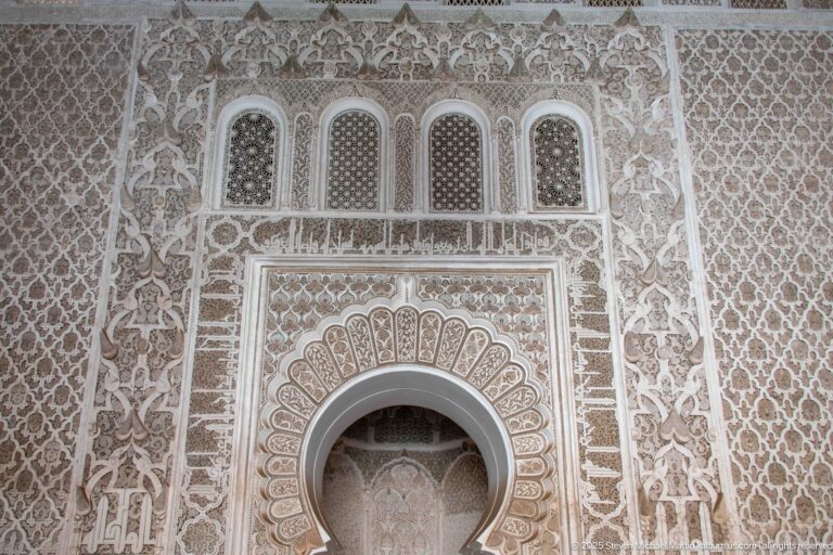 Horseshoe-arched wall niche surrounded by dense carved stucco, geometric latticework, and a row of small blind arches.