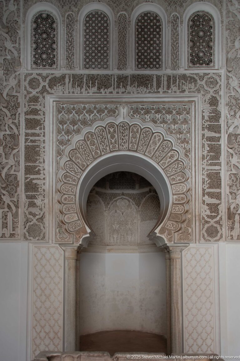 Close view of a shallow horseshoe-arched wall recess with a scalloped carved frame and three small screened openings above.