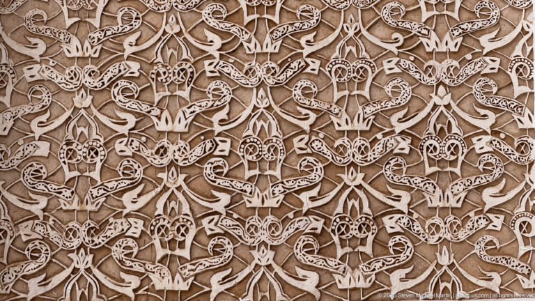 Extreme close-up of pale carved stucco filled with repeating interlaced vegetal forms and small geometric details.