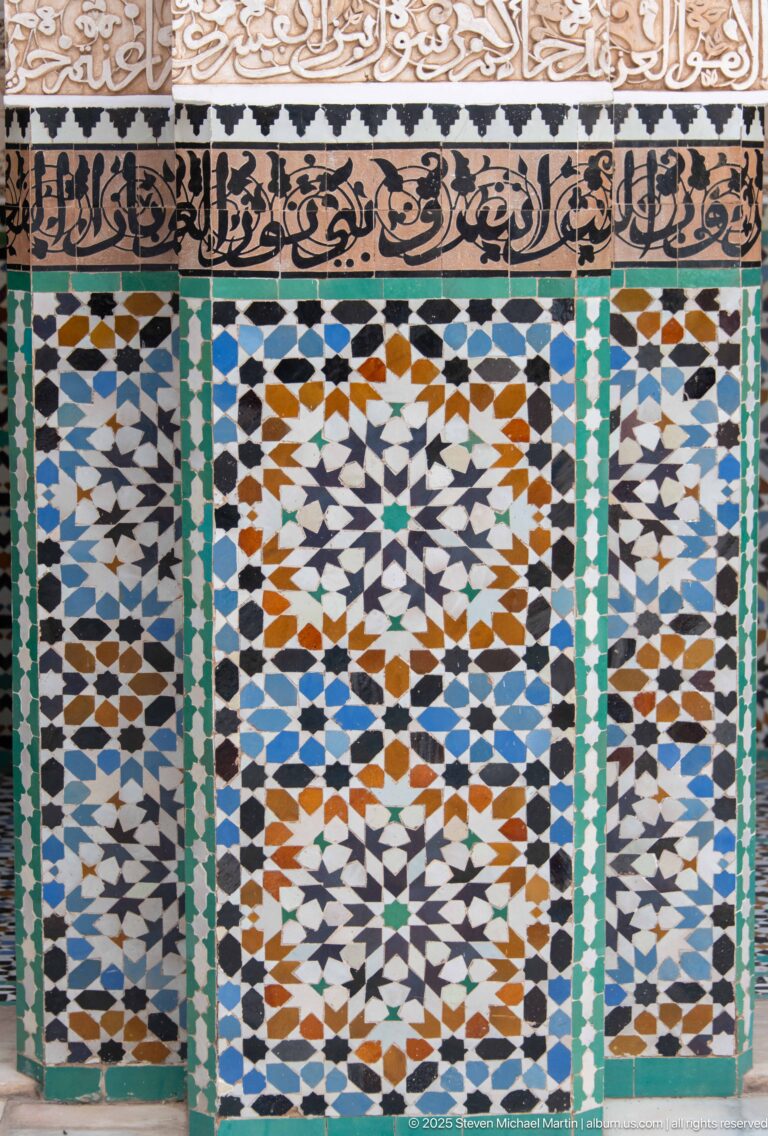 Multicolored geometric zellij panel beneath carved and painted decorative bands with Arabic calligraphy.