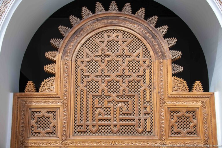 Ornately carved wooden lattice screen with geometric openwork and smaller flanking panels against a dark recess.