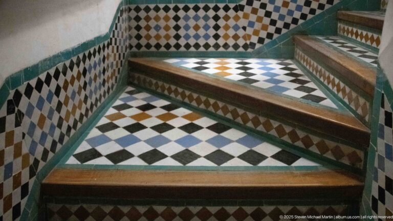 Narrow staircase covered with multicolored geometric zellij on walls, risers, and landings.