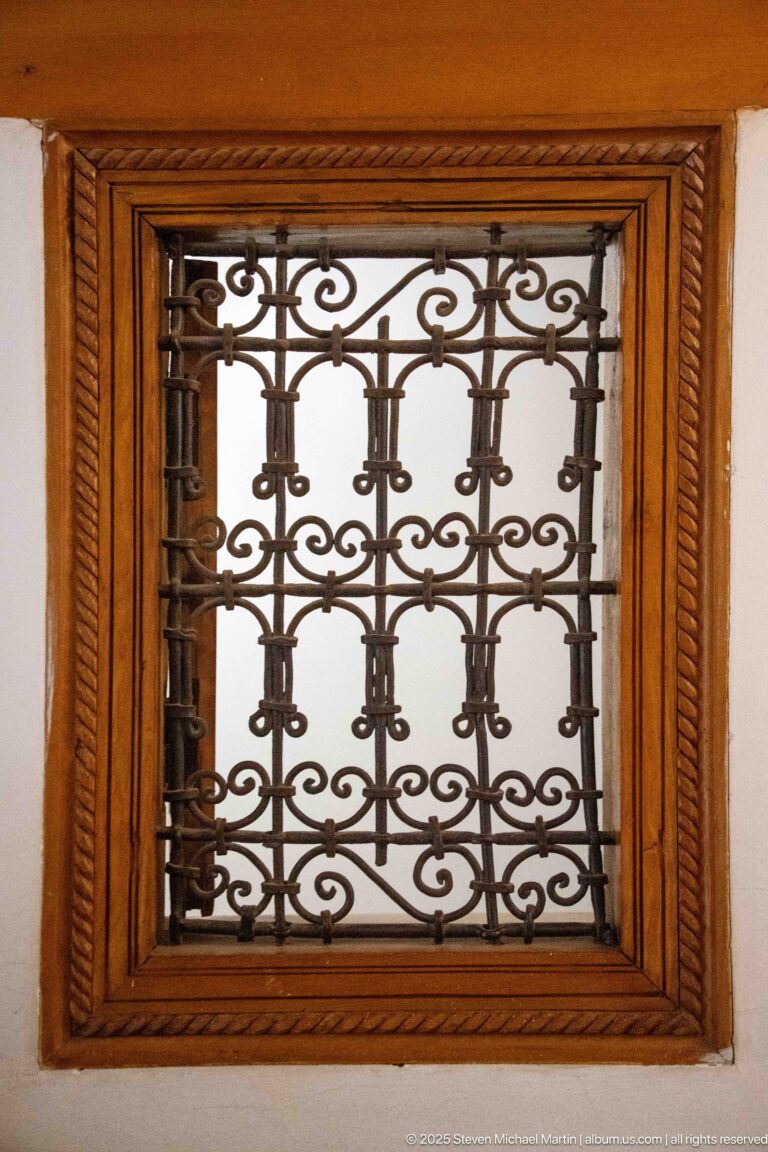 Decorative wrought-iron scrollwork grille set within a carved rectangular wooden frame.