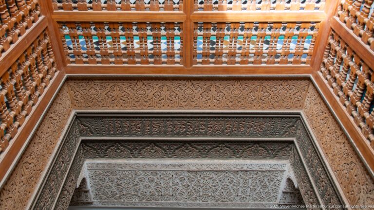 Upward view of turned wooden gallery rails above a carved stucco doorway surround.