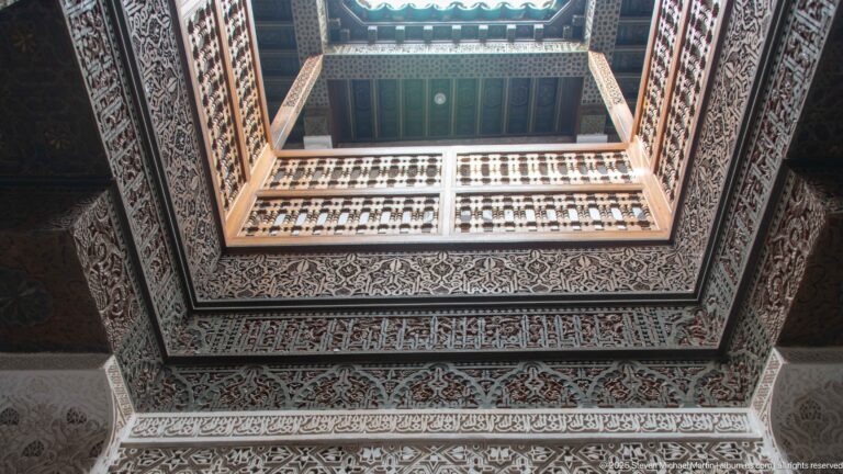 Upward view through a rectangular ceiling opening bordered by dark wood, geometric decoration, and pale carved bands.