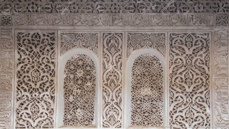 Pale carved plaster panel with two narrow arched lattice openings surrounded by interlacing arabesques.