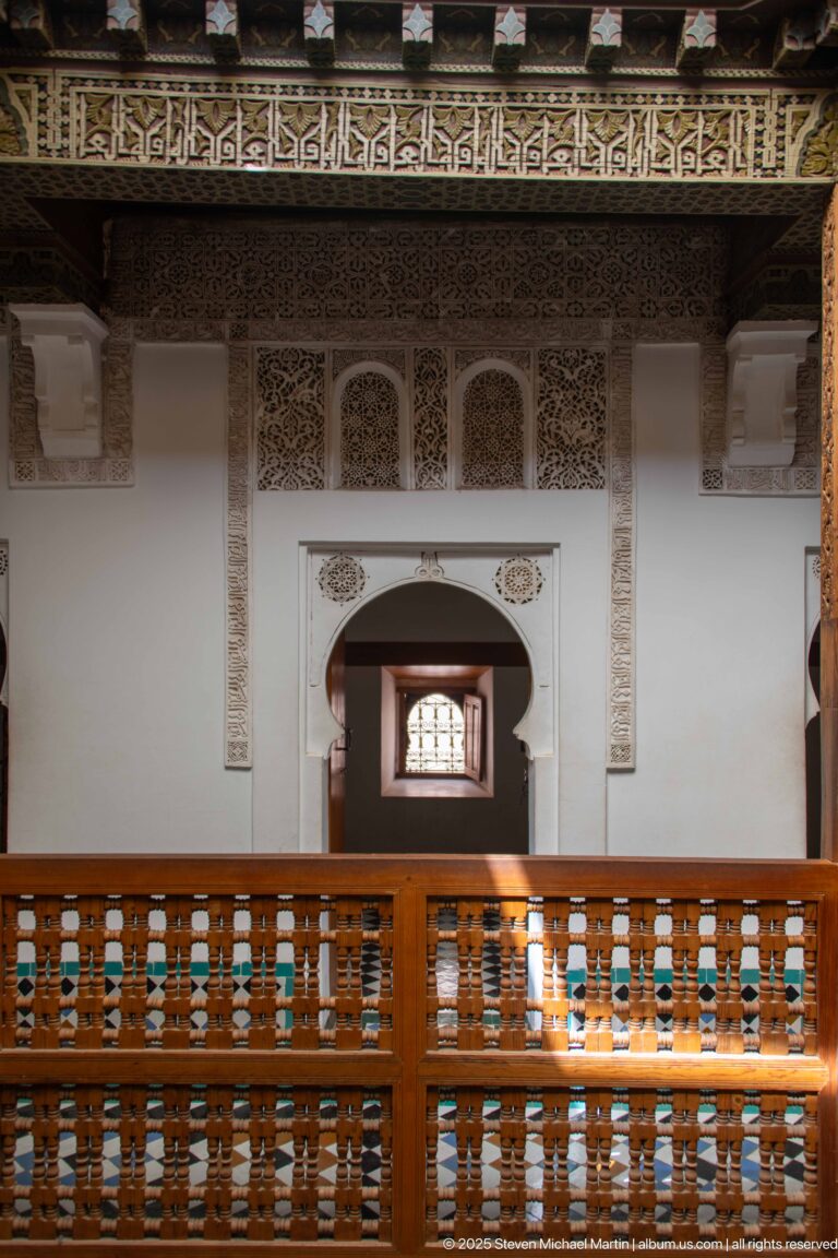 Wooden upper-gallery balustrade facing a central arched doorway with carved plaster and calligraphic trim.