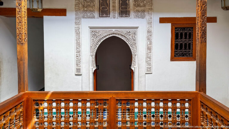 Pointed horseshoe doorway with carved plaster surround behind a wooden gallery railing and small window.