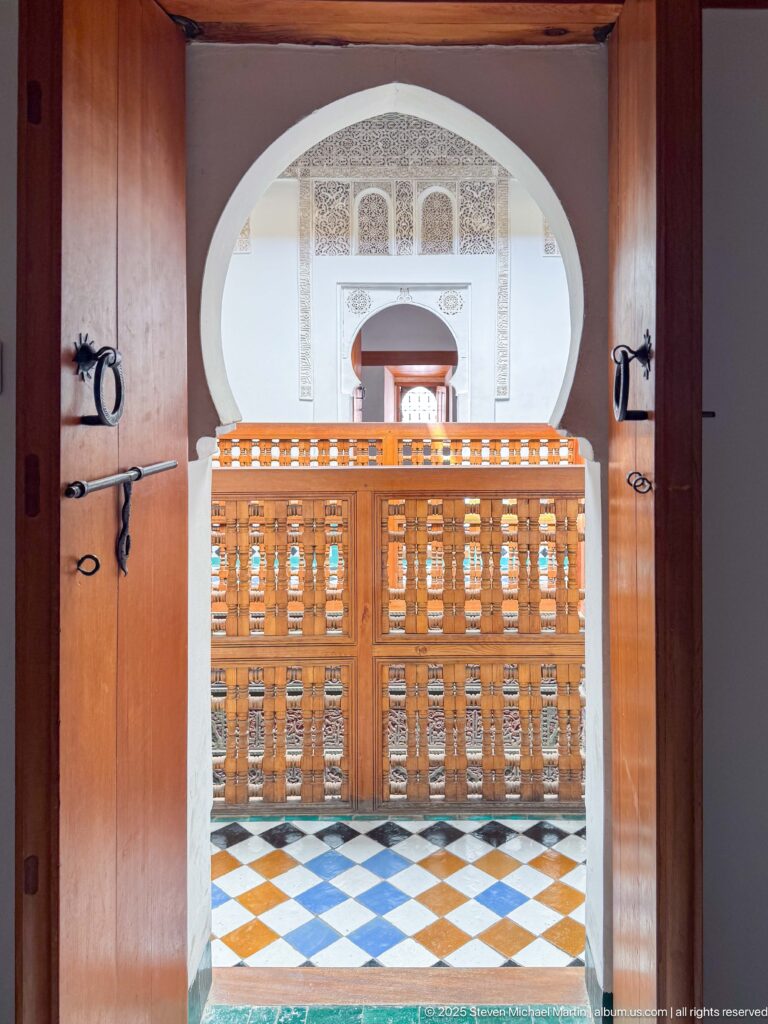 Open wooden doors framing a tiled floor, wooden gallery railing, and aligned arches beyond.