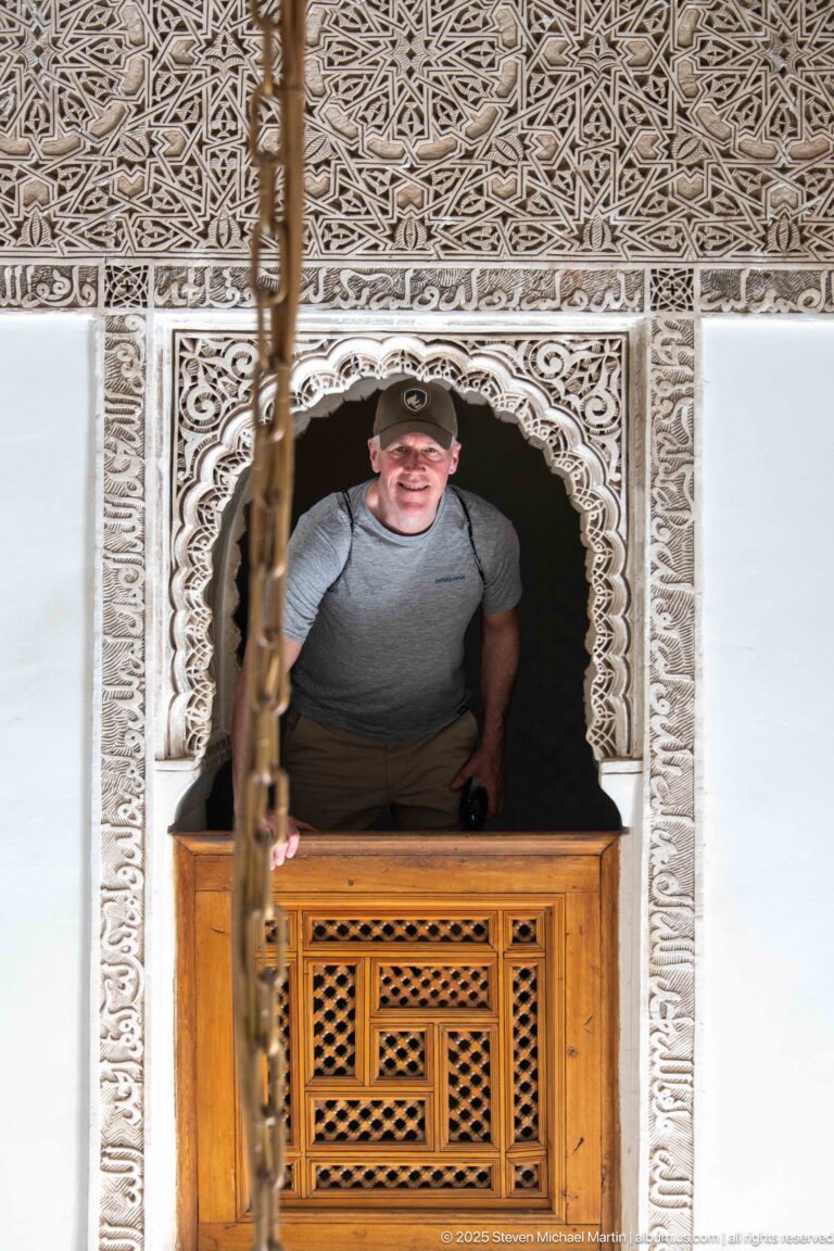 Visitor leaning through a small carved stucco arch above a wooden lattice panel.