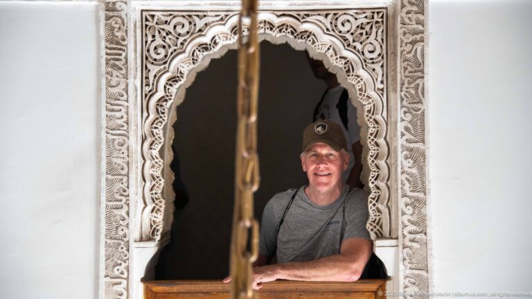 Smiling visitor in a dark recess framed by a small scalloped opening with dense carved plaster.