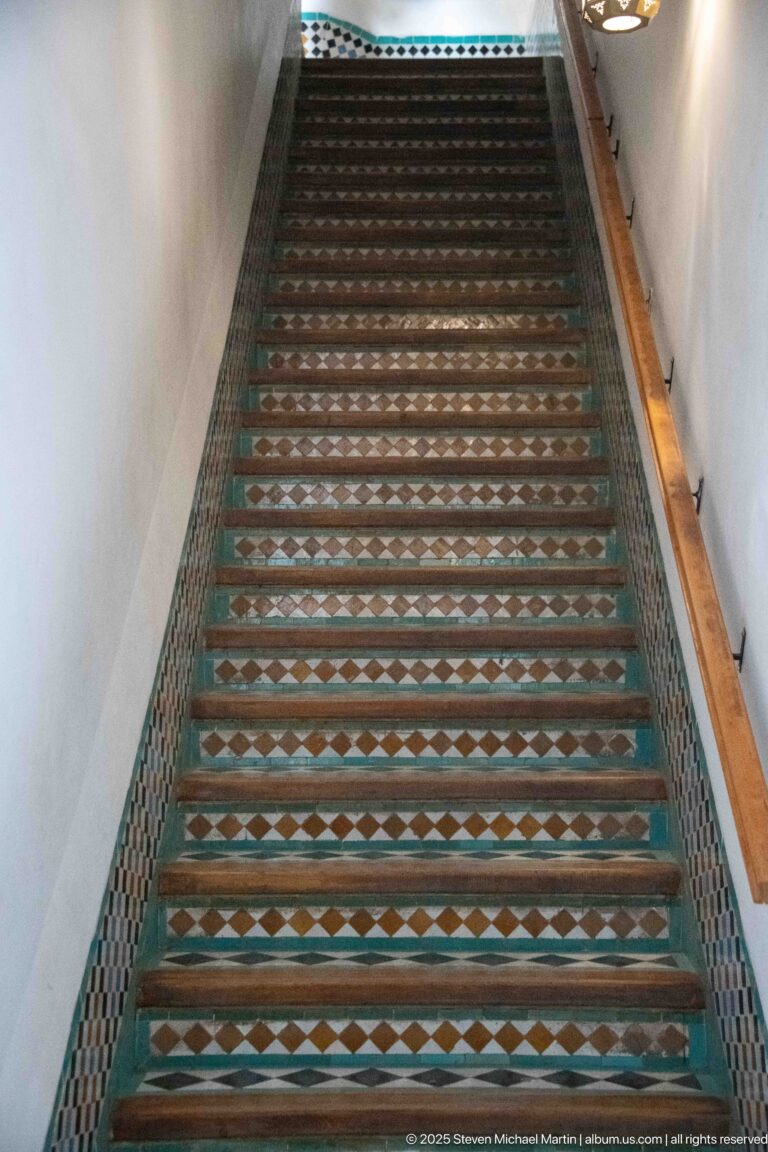 Long steep staircase with geometric zellij on risers and side borders between white walls.