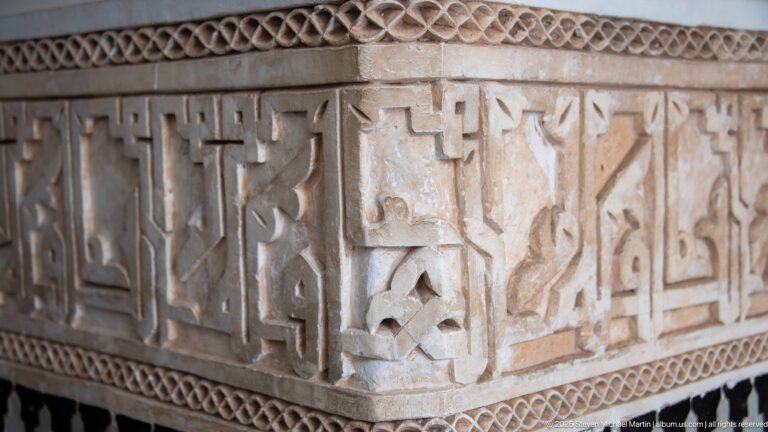 Close-up of raised Arabic calligraphy carved in pale material between narrow geometric borders, with visible surface wear.