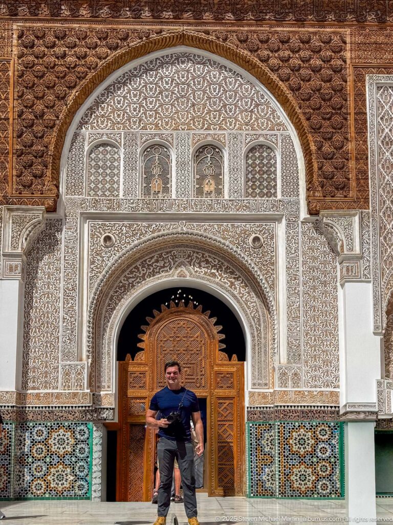 Close frontal view of an ornate courtyard portal with carved stucco arch, wooden doors, dark carved wood above, and zellij below.