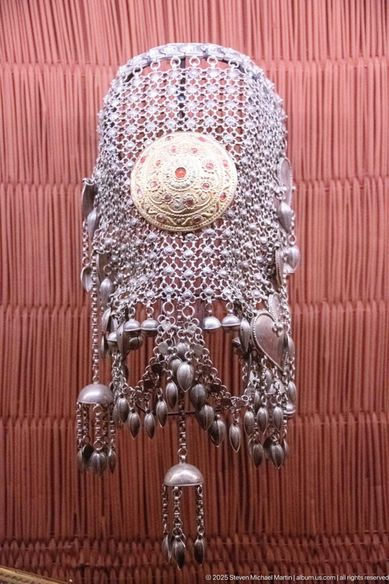 Silver-colored mesh head ornament with central round medallion, hanging chains, discs, and tubular pendants.