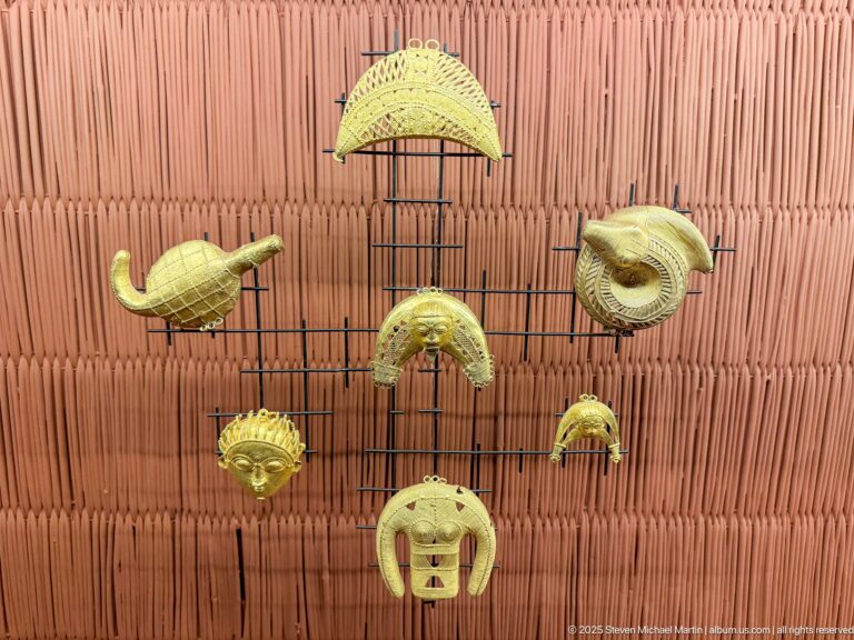 Seven gold-colored sculptural ornaments in crescent, fan, coil, and rounded forms mounted against a terracotta wall.
