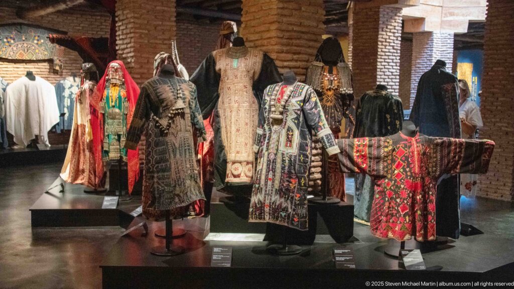 Gallery of mannequins wearing embroidered robes and tunics in dark, cream, red, and multicolored textiles.