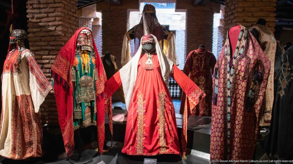 Mannequins in red, green, white, and patterned ceremonial garments, including a central veiled figure with a tall head covering.