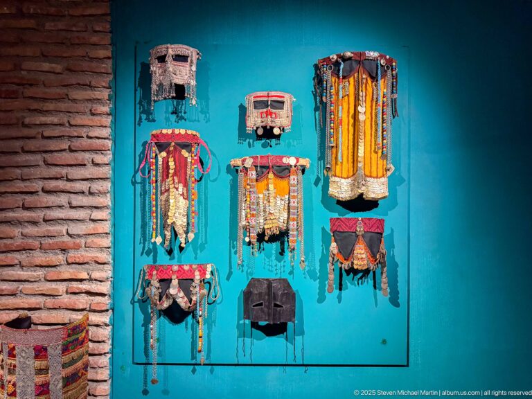 Turquoise wall displaying multiple textile and metal ornaments with tassels, chains, beads, and hanging discs.