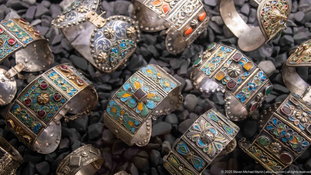 Wide metal cuffs with turquoise, blue, green, red, and orange enamel or stone-set floral decoration.