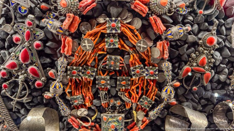 Dense jewelry arrangement of orange coral branches, silver-toned pendants, chains, and red cabochons.