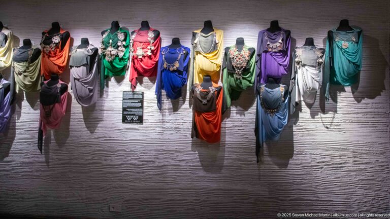 Rows of mannequins wearing brightly colored draped garments in red, green, blue, yellow, purple, white, and black.