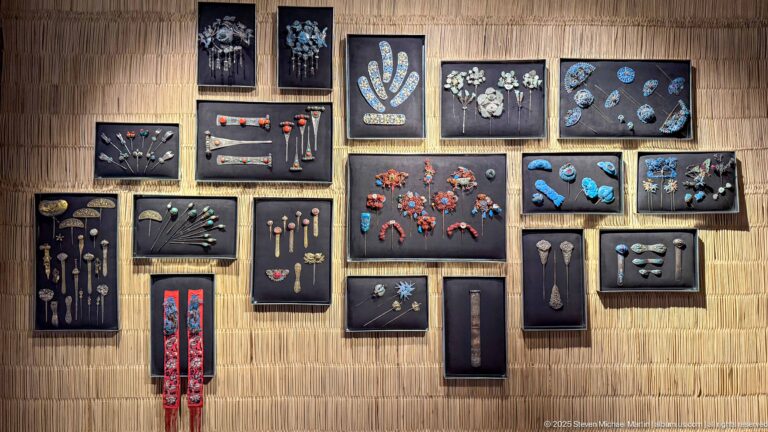 Framed groups of earrings, pins, pendants, beads, and small ornaments mounted on a woven wall.