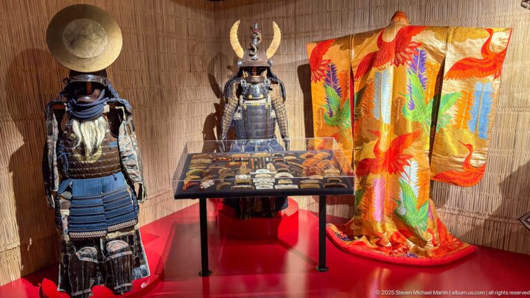 Japanese samurai armor beside an orange-gold ceremonial robe patterned with large multicolored phoenix-like birds and foliage.
