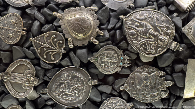 Silver-toned circular and shaped pendants with raised figures, animals, floral motifs, and patterned borders.