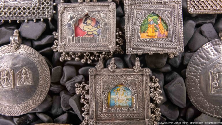 Small silver-toned framed pendants with colorful miniature paintings of figures and scenes among engraved medallions.