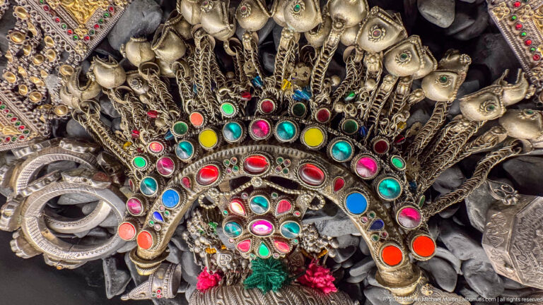 Large crescent-shaped metal ornament set with multicolored cabochons and surrounded by suspended chains and pendants.