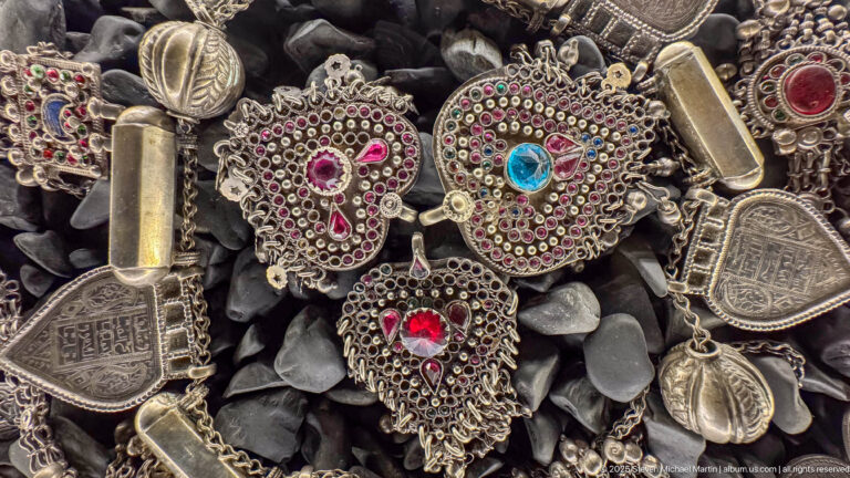 Heart-like and fan-shaped metal pendants with red and blue stones, granulated borders, and nearby amulet cases.