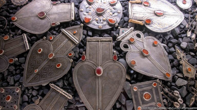 Large leaf- and shield-shaped pendants with incised geometric designs and orange-red cabochons on a dark pebble ground.