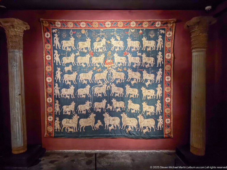 Large blue Indian devotional hanging with repeated rows of pale cattle and a broad red, cream, and blue patterned border.