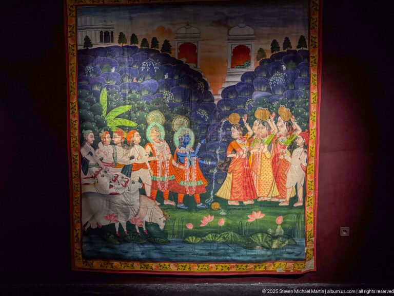 Colorful painted textile with white horses, riders, richly dressed figures, lotus-like flowers, and a dark green landscape.