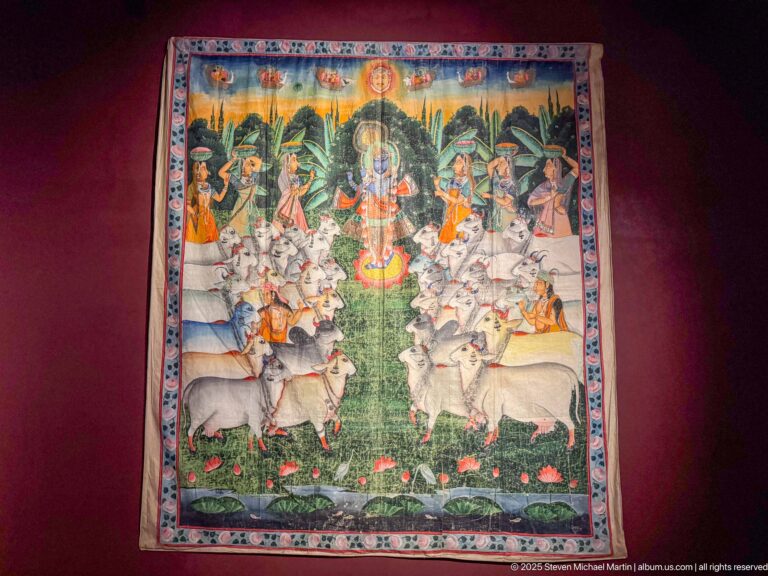 Indian pichhwai centered on Shrinathji, with attendants, rows of white cattle, floral details, and a brightly patterned border.