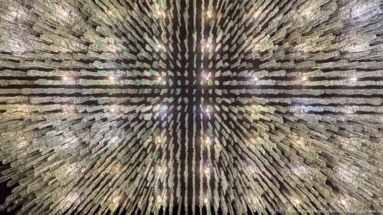 Radial wall installation of many narrow metallic elements arranged in a dense starburst pattern around a dark center.