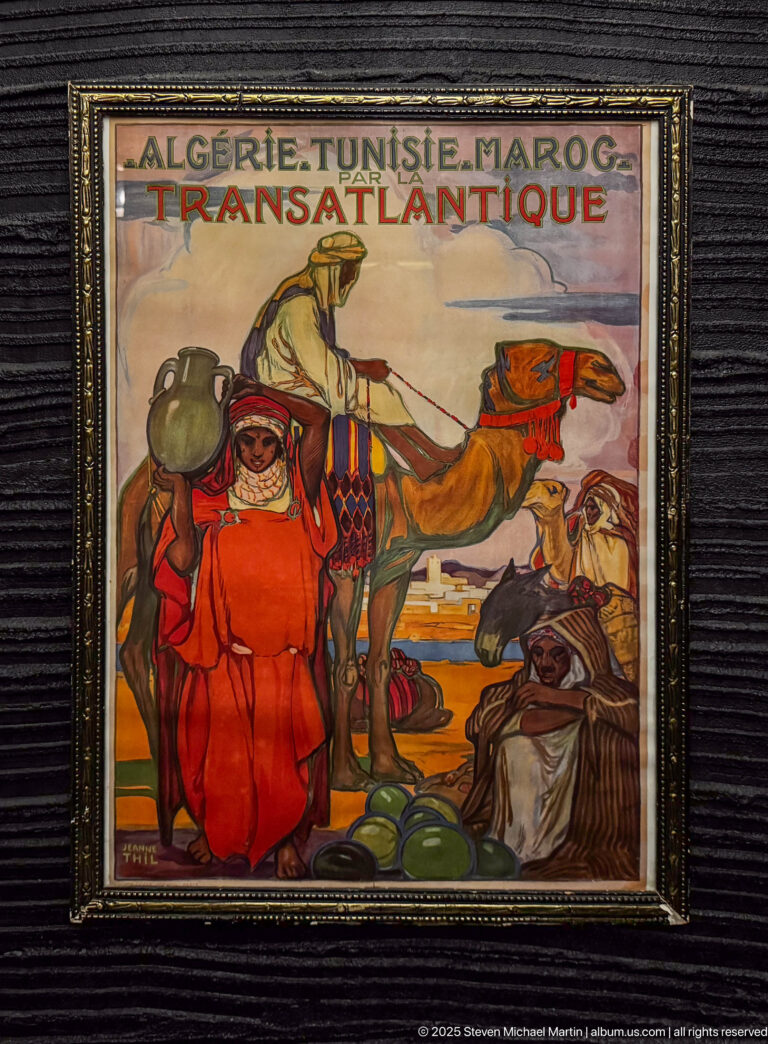 Framed vintage poster reading “Algérie Tunisie Maroc” and “Transatlantique,” with stylized figures in colorful dress and a coastal scene.