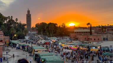 Koutoubia Mosque minaret beside Djemaa El Fna under a brilliant orange sunset.