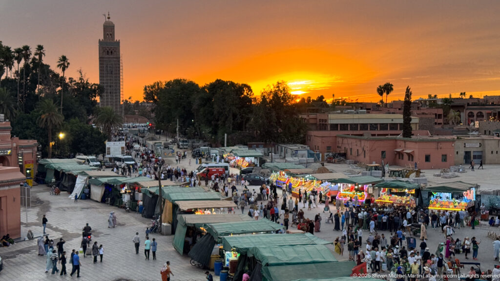 Busy Djemaa El Fna market stalls and pedestrians beneath an orange sunset and silhouetted palms.