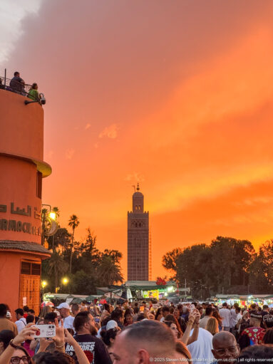 Koutoubia Mosque minaret rising above a dense crowd under an intense orange evening sky.