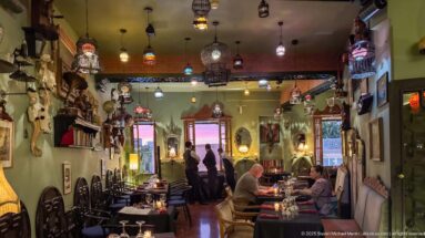 Narrow Le Marrakchi dining room with colorful hanging lanterns, diners, green walls, and decorated tables.