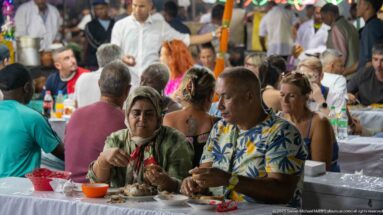 Man and woman eating at a crowded communal table in a Jemaa el-Fna food-stall seating area.