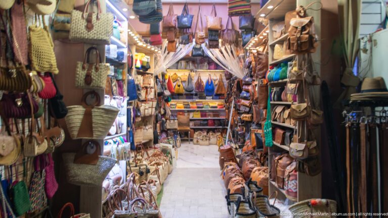 Narrow Marrakech shop densely packed with leather bags, satchels, belts, slippers, and small accessories on both walls.