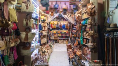 Narrow Marrakech shop densely packed with leather bags, satchels, belts, slippers, and small accessories on both walls.